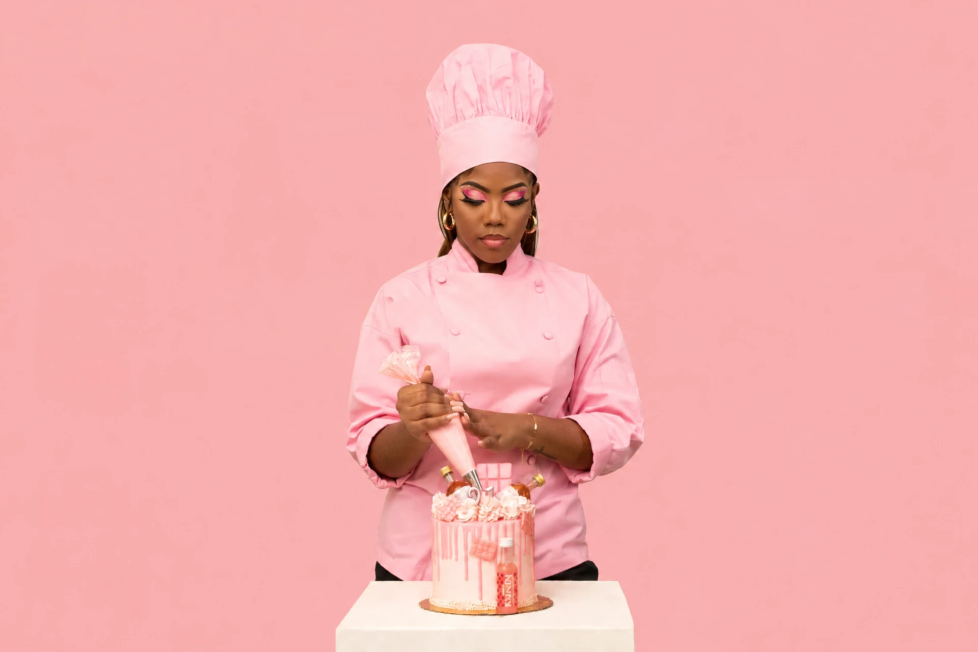 J'Dawn of The Baker Mom in a pink chef jacket piping a pink celebration cake
